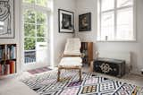 Bamboo chair with fur throws sits atop yellow, pink, and black diamond patterned rug near a black antique chest.