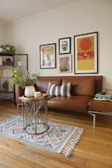 The studio's main room features original wood flooring and accent rug. A wall of framed artwork hangs up the brown leather  sofa.