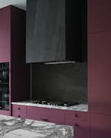 The range hood and backsplash are clad in a charcoal stone tile, contrasting with the light countertops and plum colored cabinets.