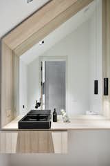 At a family compound in Nantucket, the materials in the restroom speak to the local vernacular, with wood paneling and countertop, but the minimalist detailing and light finish make it modern. The black sink and accessories contrast against the white walls, adding another dimension.