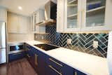 the golden handles on the blue cabinets make the deep blue herringbone patterned back splash stand out even more