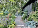 Back up front, a serpentine pathway leads to the dogtrot. Embedded stone plinths repeat the building's vertical siding.