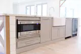 Detail of drawer style microwave, oversized farmhouse sink, wine fridge. Abundant natural light.