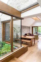 Harefield Road East - A planted courtyard sits centrally within the ground floor plan, offering an integral urban oasis to a South London semi-detached house.

The client, a family of three, had just returned after living for a period of time in Sydney when Gruff Architects were approached to refurbish and extend their Victorian semi in South London. Keen to recreate the benefits of the outside lifestyle and warmer climate they had experienced abroad, whilst incorporating their mixed heritage into the design, the client instilled Malaysian, British and Australian influences into the brief. Set in the Brockley Conservation Area, the extension includes a kitchen, utility and dining space for the family and focuses on creating a connection to the leafy garden.  
Gruff’s design focuses on a centrally planted courtyard which sits between the original house and new extension, connecting the two elements together and bringing natural light and soft planting into the heart of the building. Working with Michael Coley Garden Design, the planting features neutral, evergreen and hardy plants for longevity as well as larger pieces to add focus, such as the tree fern. 

Toward the rear of the extension, a section of corner glazing further punctures the centre of the building, allowing direct sunlight and more visible planting to enter the floor plan. Study spaces, mirrored either side of the internal courtyard, look out onto the planting and provide a visual relationship between both the existing and new architecture as well as the internal and external environments all year round, without the need to open doors or windows. In warm weather, however, the timber glazing allows for the space to be opened up to the planted areas and encourages cross-ventilation to naturally cool the home.

A combination of natural timbers, exposed grey brickwork and pockets of glazing appear both inside and out, blurring the thresholds and creating a calming environment. New openings combined with glazed partitions, create a light and inviting environment across the whole house and a statement pitched roof frames a full-length flat rooflight to the ridge of the extension, creating views up to the sky from within the dining area.


Rhys Cannon Director at Gruff Architects 
‘Our client’s brief, to replicate the outside lifestyle of a warmer climate, set an interesting opportunity for us. Located in London, we challenged the lack of outdoor-living by sitting a fully glazed courtyard centrally within the plan of the house. Inserting elements of ‘garden’ into the building footprint, blurs the inside with the outside by offering moments of interaction with planted, naturally lit areas.’
