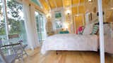 Bedroom, Medium Hardwood Floor, Chair, Wall Lighting, Bed, and Bookcase From glass door entrance  Photo 4 of 11 in Romantic Tree Cottage in the Hawaiian Rainforest by Shannon Victoria