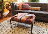 The ottoman coffee table is upholstered in a Turkish kilim. The golden throw pillow is made from recycled Indian saaris. The red and purple pillow is Cambodian silk. The yellow and gray pillow is Anatolian silk from Turkey and features tribal figures.