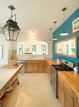Kitchen, Refrigerator, Wood Counter, Wood Cabinet, Range, Accent Lighting, Dishwasher, Vinyl Floor, Light Hardwood Floor, Drop In Sink, and Pendant Lighting Modern Farmhouse kitchen.   Photo 15 of 22 in Contemporary Vermont Farmhouse by Lindsay Selin Photography