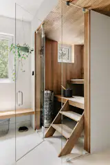 Japandi inspired bathroom featuring minimalist white oak floating vanities with true terrazzo tile on the floors and white finger tiles on the walls. Included in this space is a traditional Finnish sauna made out of thermotreated aspen from Finland