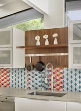 The kitchen features crisp, white cabinets, colorful mosaic tiles, and walnut accents. 