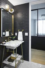 Modern Seaholm Powder Room in downtown Austin condo. Featuring a Carrara marble vanity with brass hardware, black tile brick walls and scalloped floor tile. 