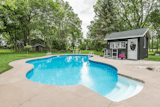 Large custom pool with concrete deck, pool house and river rock gardens. There is a large barn and shed in the background outside the pool enclosure.