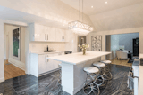 Kitchen The large kitchen has black zebra marble flooring with a 9ft white quartz island and counter tops. The cabinetry is custom white high gloss featuring high end appliances including a 36 inch gas stove and a rectangle crystal light fixture. This room adjoins the fireplace room and a large pantry area with floor to ceiling storage in the same high gloss cabinets. The art is Canadian native by Christian Morrisseau in the black and white colour scheme. There is a large wooden deck through the glass door off the kitchen for out door dining .  Photo 6 of 10 in The Empress by Peggy Aleksiejuk