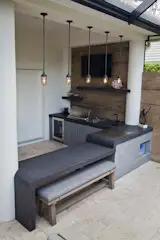 Modern outdoor kitchen constructed of glass fiber reinforced concrete (GFRC) with 4" double waterfall countertop. Kitchen includes seating with pendant lights overhead, decorative niche, teppanyaki grill, sink, gas grill and refrigerator. Privacy wall featuring wood-look porcelain tile, floating shelves and television and accent lighting.
Photo by Vania Hardtle