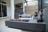 Seating area with modern gas fire feature. Surrounding walls of glass fiber reinforced concrete (GFRC) with integrated custom aluminum lighting. Outdoor kitchen constructed of GFRC with 4" double waterfall countertop. Kitchen includes seating with pendant lights overhead, decorative niche, teppanyaki grill, sink, gas grill and refrigerator. Privacy wall featuring wood-look porcelain tile, floating shelves and television and accent lighting. Furniture and fire feature by Restoration Hardware.
Photo by Vania Hardtle