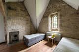 With its vaulted ceiling, tall narrow window, and exposed stone walls, this bedroom has the feeling of a convent or church building. 