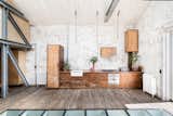 The kitchen area is full of charm, with cabinets made from reclaimed Iroko wood, incandescent lightbulb-style pendant lights hanging above the units, and a collection of potted house plants.