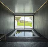 Bath, Stone Slab, Slate, Drop In, Recessed, Soaking, and Dark Hardwood With dark gray tiles that mimic stone and atmospheric lighting, this cave-like space has a soothing feel while evoking elemental landscapes. The picture window provides scenic views of the garden, grassland, and the hills beyond while you relax in the spa bath.  Bath Stone Slab Drop In Photos from A UK Home With Panoramic Ocean Vistas Asks $3.5M