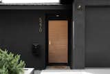 The dark facade is contrasted by Pom Pom olive trees and a warm solid wood door with brass Emtek hardware