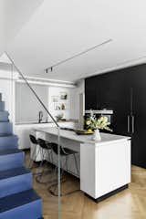 In an apartment renovation in Tel Aviv by Maya Sheinberger, a white and black kitchen comes together in a white island with black base and black bar stools by infiniti.