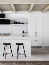 A marble island and white cabinetry define the bright, open kitchen, while matte black and bronze finishes celebrate craftsmanship.