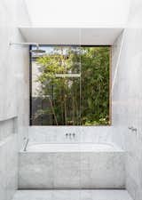 Bathroom features Carrara Marble flooring and walls. Window slides open on to garden foliage.