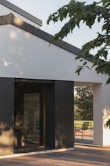 Detail of the façade where steel shutters integrate seamlessly into the white volume, enhancing the minimalist aesthetic. The interplay of natural light and shadows adds depth and movement to the architectural composition.