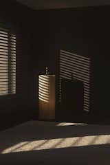 Interior of the master bedroom, where light and shadow interact through Venetian blinds, creating a dynamic yet serene atmosphere. The DORA floor lamp by SANTA & COLE adds a warm, sculptural presence, enhancing the intimate ambiance of the space.