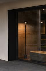 Detail of the glazed façade, where Venetian blinds filter the warm interior light. Inside, the Peak floor lamp by Francesc Rifé for Milan Iluminación adds a subtle yet elegant touch, enhancing the serene and refined atmosphere of the space.
