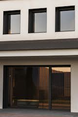 Facade detail showcasing the geometric precision of the openings, framed in black to contrast with the white volume. The large sliding glass doors reflect the landscape, reinforcing the seamless dialogue between interior and exterior spaces.