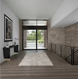 The highlight of the foyer in this Franklin home, completed in 2017, is the large entry door which features a 9 foot high by 6 foot wide panel that pivots open.  The door is constructed of rift cut white oak and glass along with a matching transom above.  An Indiana limestone wall rises 20’ from the lower level to the ceiling of the foyer.  This wall comes in from the outside interrupted only by the jamb of the custom entry door.  There is also a subtle drywall reveal featured along the edge where the walls meet the ceiling.  The simple and uncluttered steel rail features a design requested by the owner to tie into the recurring linear theme throughout the homes interior and exterior.  The expansive foyer showcases the wide plank French oak floor that is used throughout the main floor of the home.   