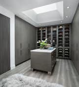 The owners of this Franklin home, completed in 2017, wanted a fitted closet with no exposed hanging or shelving but with a lot of drawers in place of a conventional dresser or armoire in the bedroom itself.  The glass doors are both functional and beautiful allowing one to view the shoes and accessories easily and also serves as an eye-catching display wall.  The center island, with a quartz countertop, provides a place for folding, packing, and organizing with drawers accessed from both sides.  Not shown is a similar half of the closet for him and a luggage closet.  The designer created splayed shafts for the large skylights to provide natural light without losing any wall space.  The master closet also features one of the flush doors that were used throughout the home.  These doors, made of European wood grain laminate with simple horizontal grooves cut in to create a paneled appearance, were mounted with hidden hinges, no casing, and European magnetic locks.  