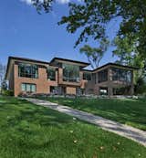 This home in Franklin, completed in 2017, was inspired by the Frank Lloyd Wright Robie House in Chicago and uses linear design materials including large overhangs and a shallow sloped hip roof.  The exterior materials feature a norman style brick with colored mortar, tooled horizontal joints, and filled vertical joints, as well as long pieces of Indiana split-faced limestone in varying heights.  The siding and fascia are wire-brushed African mahogany with a smooth mahogany reveal between boards.  The windows are full height to the bottom of the stuccoed soffits that also feature hidden ventilation.  The motor court features a combination of exposed aggregate and sawcut concrete while the entry steps are porcelain tile.  The magnificent white oak and glass entry system continues the horizontal linear theme.  The metal edges on the roof conceal gutters while downspouts are hidden inside the structure leaving a clean roofline.  The house is situated on a hill that rolls toward the lake and features a walkout lower level giving it a two story appearance in the rear.  The 12’ high dining room windows in the center of the house are framed in African mahogany with a larger overhang.  The large kitchen window and floor-to-ceiling windows in the master bedroom and sitting room, tucked beneath the ample overhangs, complete the look.
