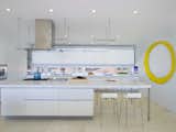 This light, airy, state-of-the-art kitchen sits at the front of the home, looking into the living area. Gaggenau appliances pair with a dramatic, stainless-steel oven hood. A bright yellow wall sculpture by Brad Howe channels the sun, adding visual interest, while white Corian countertops keeps the space feeling sleek.