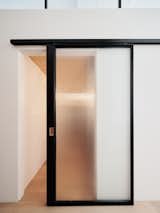 Custom steel and fluted glass barn doors provide privacy to both the office and the adjacent den, while also allowing shared light from the large fenestration at the main living space to filter through.