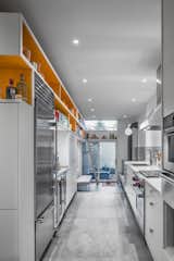 This renovation project transformed a dark, cramped kitchen into a light-filled, well-organized space that steps down into a newly added lounge area bordering the garden. The skewed bar of orange shelving provides deep storage in the kitchen and narrows to 'knickknack' depth in the lounge.