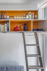 The skewed band of overhead orange shelving that blazes a trail through the kitchen and lounge provides storage space for the owner who loves colour collecting things – and organizes objects in a way that pleases her minimalism-inclined partner.