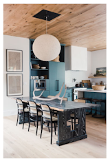 In the kitchen, tatement lighting by Nuevo Living, teal appliances, and an intricately-carved wooden table juxtaposes modern living with rustic touches.