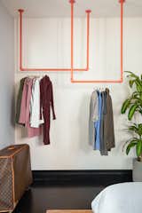 Clothes are hung on an inviting set of orange-painted pipes in the guest bedroom.