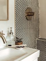 The bathroom has an earthy vibe thanks to greenery and a shower covered in muted penny tiles.