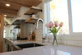 The kitchen features a large sliding window, stainless apron front sink, sparkling quartz counter tops and a modern pull down faucet. The abundance of counter space is key  in this L-shaped kitchen. 