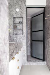 Grey marble, white wood, black metal and glass doors, along with brass accents, creates a contemporary and calming master bathroom.