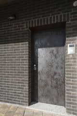The main entrance door is coated with a “rusty brown” metal to merge wiht the dark brick facade.