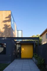 The exterior walls on the first floor of Virginia House by 2712 / Asociados are painted in a dark, neutral color that contrasts with the bright illuminated interiors and sunny yellow front door.