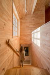 The wooden staircase of Tarusa House features a large street-facing window. Wood covers the floor, ceiling, and walls in most of this home designed by Architectural Bureau Project 905.