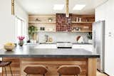 Natural wood and earth tones fill this light filled kitchen. Textured brown zelige tile wraps the hood, which sits against a grey subway tiled backsplash, while grey quartz countertop offer tons of counter space.