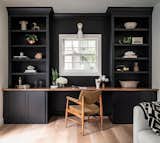 The dark black shelving of the office wall contracts strikingly with the light flooring and furniture, creating a sense of depth.