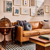 Mediterranean mets stately fair in this living room with pops of blue and gold through a custom art wall, striped rug, vintage coffee table, antique globe bar, and leather sofa.