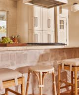 Close up of the kitchens long island with textured stone, mix and matched counter stools, open range, and custom stained exposed beams.