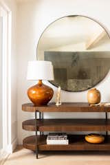 Dark wood and black metal media console with large round industrial mirror, and vintage amber lamp.