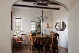 Dining room with round dining table and antique chairs, a black matte chandelier, seating in the corner, and exposed painted beams. A cut out looks into the kitchen and opens the space.
